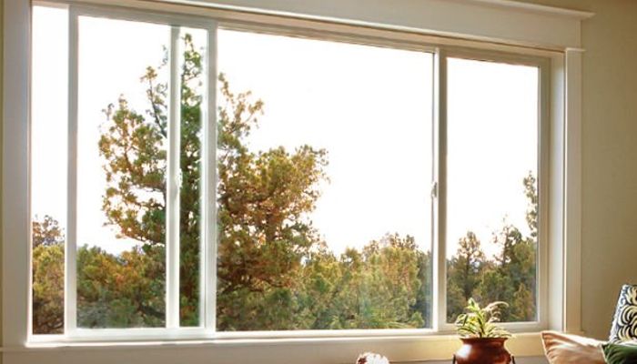 Large white sliding window overlooks a vibrant forest of green and autumn-colored trees.