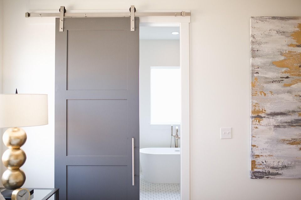 Modern gray barn door on a steel track revealing a contemporary bathroom with a tub.
