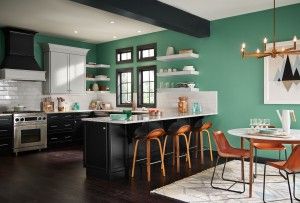 Modern kitchen with green walls, black cabinets, white countertops, and wooden bar stools.