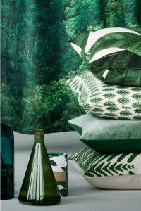 Stack of green pillows with leaf patterns, alongside green glass bottles and a forest background.