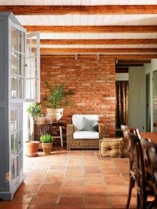 A rustic living space with terracotta floor tiles, exposed wooden beams, and a brick accent wall.