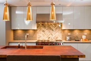 Modern kitchen featuring a large wooden island, three gold pendant lights, and a herringbone backsplash.