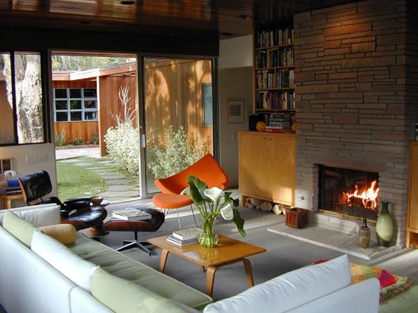Modern living room with a lit fireplace, white sofa, and lush backyard view.