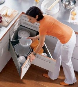 Woman organizing white and orange dishes in a pull-out corner kitchen cabinet.
