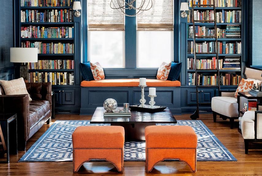 A cozy living room with dark blue built-in bookshelves, an orange window seat, and comfortable seating.