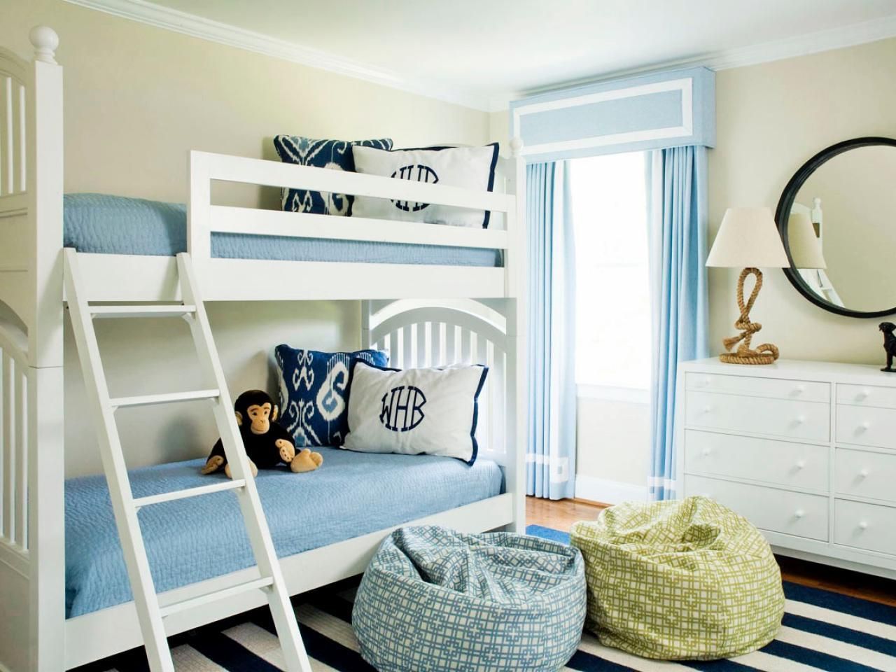 White bunk beds with blue bedding, a striped rug, and bean bag chairs in a bright room.