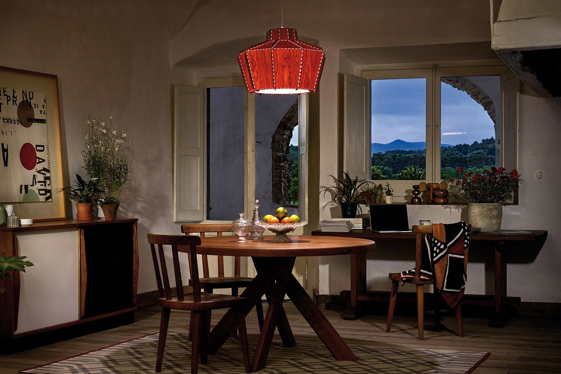 Cozy dining room with a red pendant light, wooden table, and scenic window view.