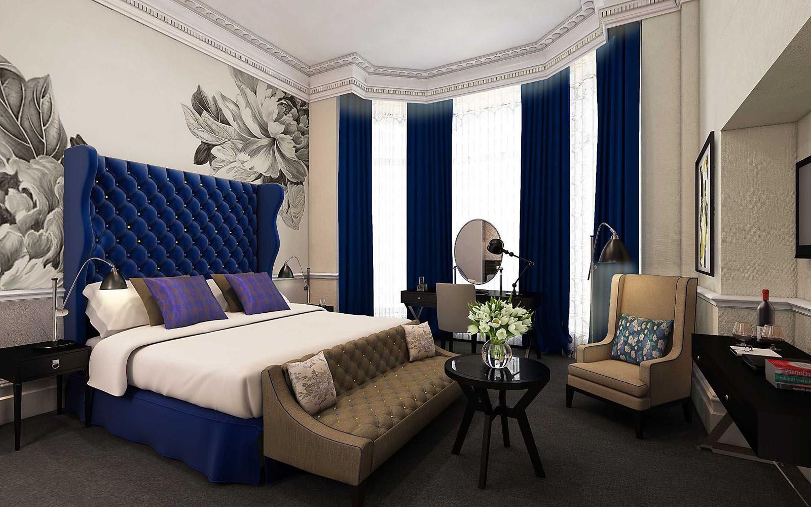 Luxurious hotel bedroom with a blue tufted bed, striped curtains, and floral wallpaper.