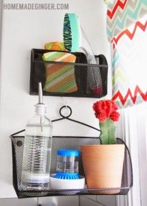 Two black mesh caddies hold dish soap, sponges, scrub brushes, and a red cactus.