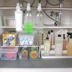 Organized under-sink cabinet with clear bottles of cleaning supplies and various containers.