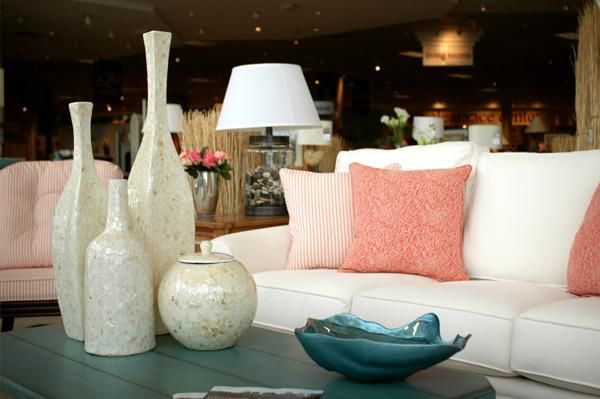White sofa with pink and coral pillows, decorative white vases on a coffee table.