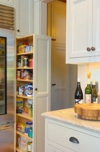 Slim pull-out pantry organizer filled with various food items next to a stainless steel refrigerator.