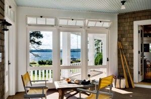 Enclosed porch with large windows overlooking a scenic blue lake and green trees.