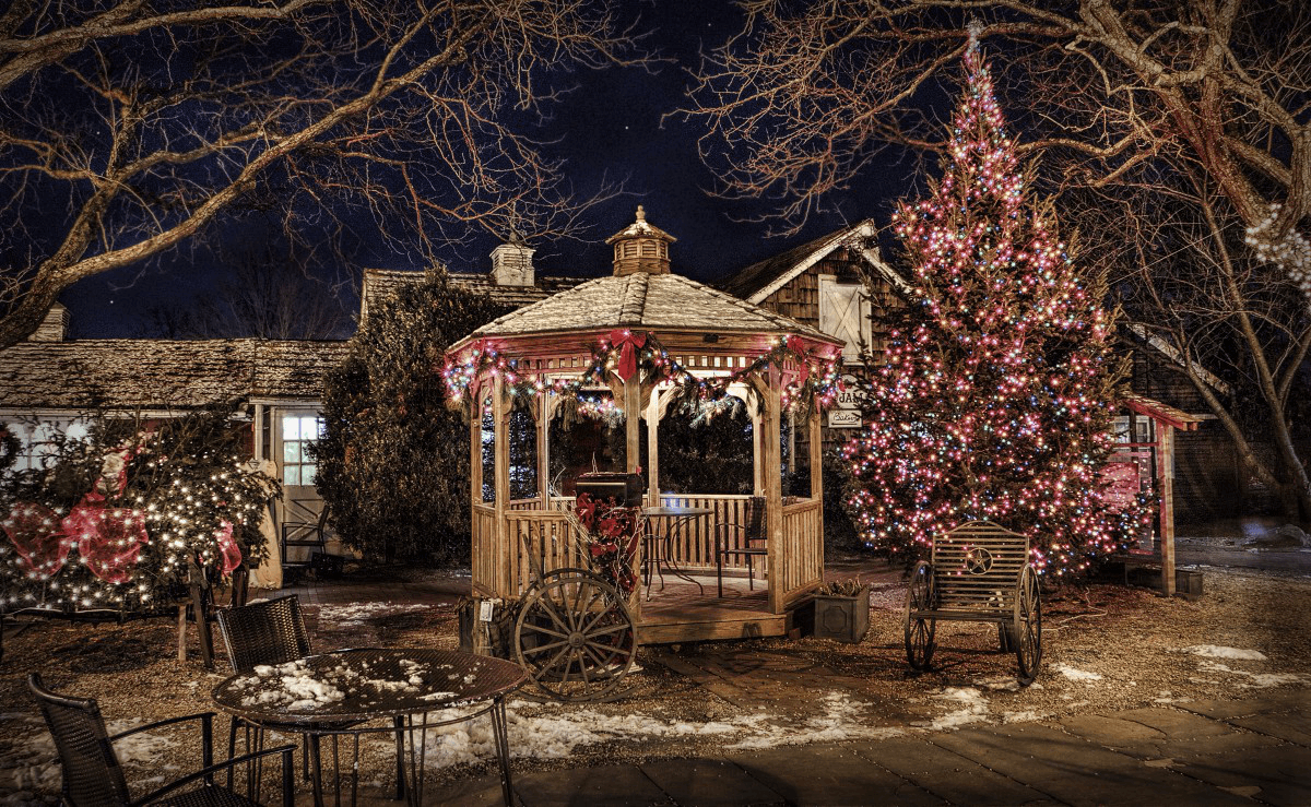 Festive outdoor scene at night with a decorated gazebo and large Christmas tree.